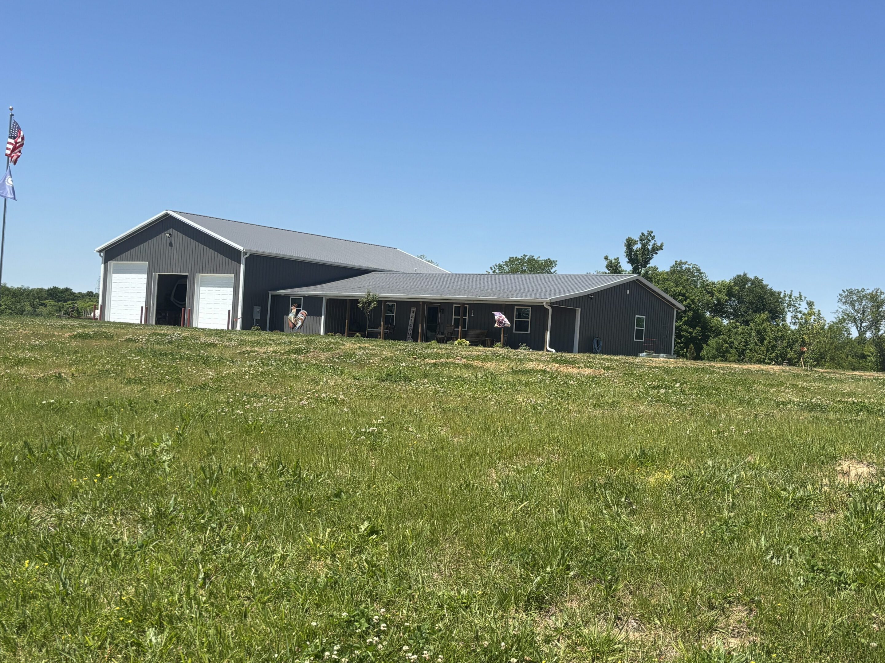 Large gray metal barn with porch and flags